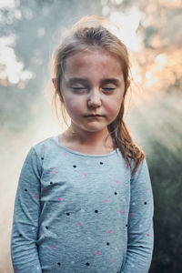 Portrait of sad little girl with closed eyes standing in smoke back to sunlight