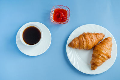 Croissants with jam and morning coffee flat lay. isolated on blue background.