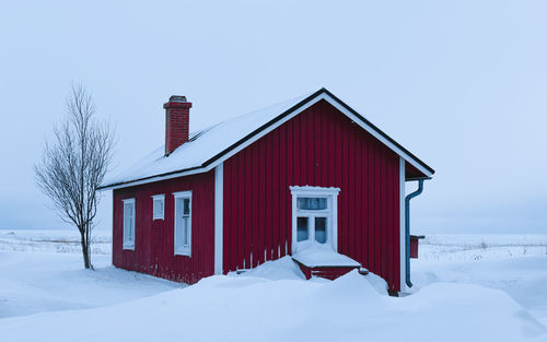 House on snow covered field against clear sky