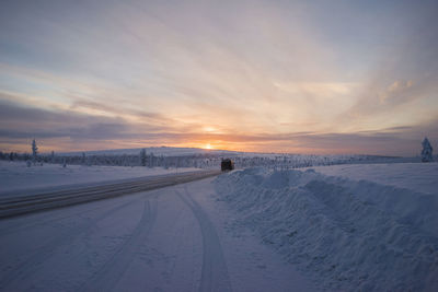 Snow covered field against sky during sunset