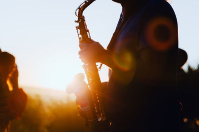 Midsection of man playing saxophone against clear sky during sunset