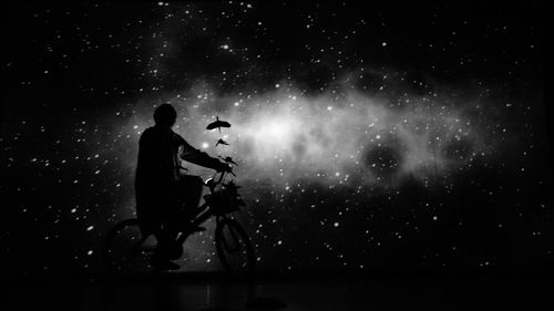 Silhouette person with bicycle against star field