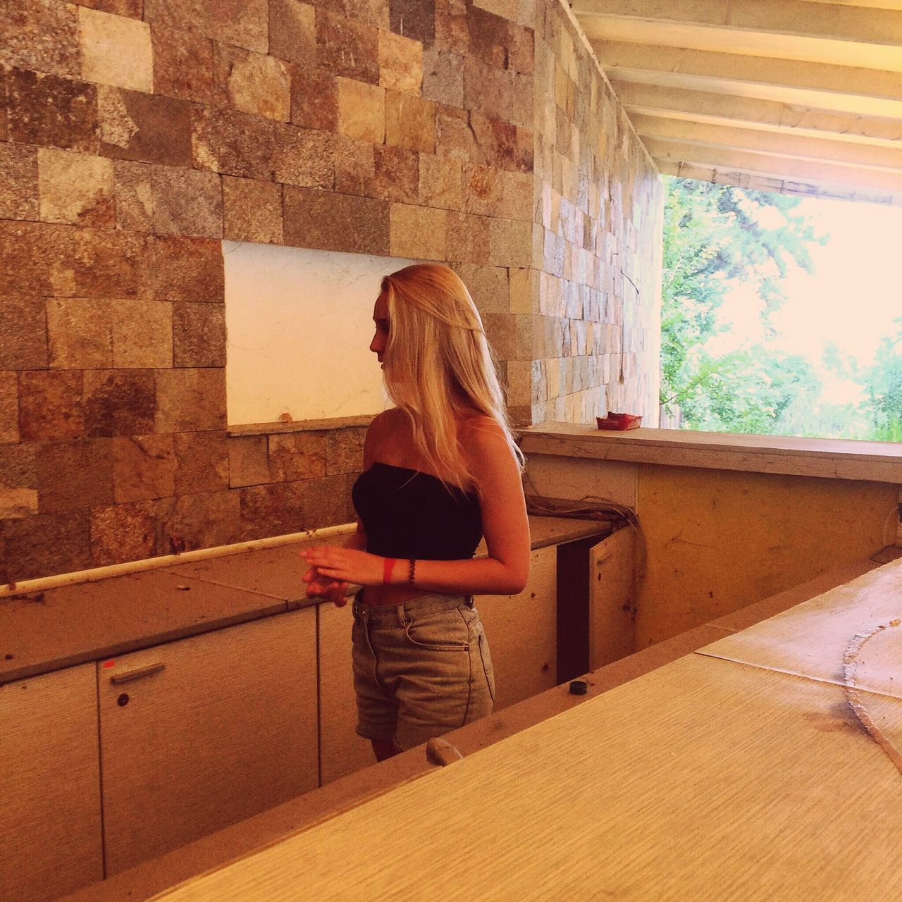 REAR VIEW OF WOMAN STANDING AGAINST WINDOW IN WALL