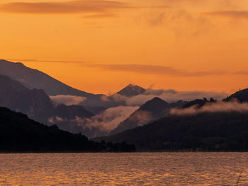 Scenic view of lake by silhouette mountains against orange sky