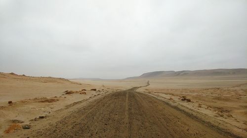 Dirt road passing through desert against sky