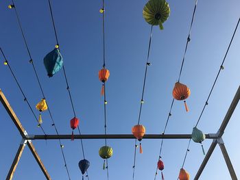 Low angle view of hanging lights against clear blue sky