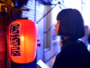 Side view of woman by chinese lantern in city 