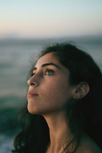 Portrait of young woman looking away against sky