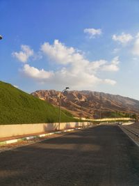 Empty road leading towards mountains against blue sky