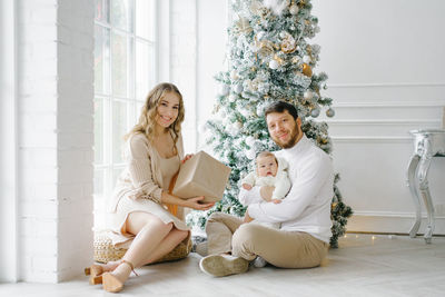 Beautiful happy family sitting on the floor near the christmas tree in the bright living room. 