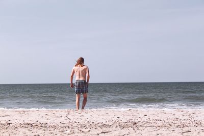 Rear view of shirtless man walking at beach against sky
