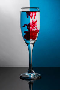 Close-up of red ink in wineglass on table against colored background