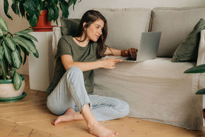 Young woman using digital tablet while sitting on sofa at home