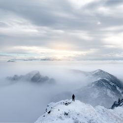 Person standing on snowcapped mountain against cloudy sky