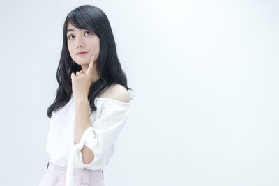 Portrait of young woman standing against white background
