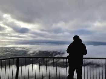 Rear view of silhouette man standing by railing against sky