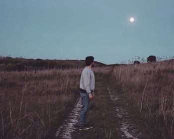 Side view of man standing on grassy field against sky at dusk