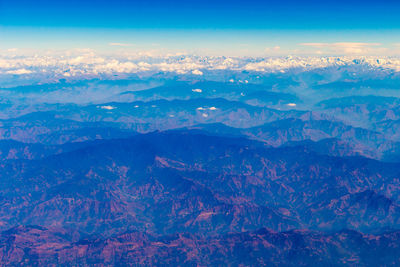 Aerial view of snowcapped mountains against blue sky