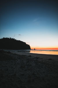 Scenic view of beach against clear sky at sunset