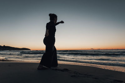 Silhouette woman standing on beach against sky during sunset