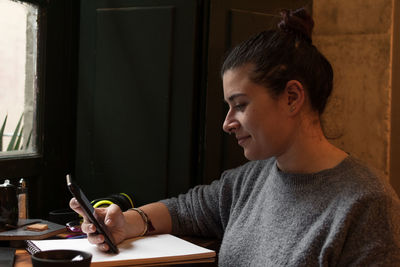 Young woman looks at her phone while studying in a retro pub