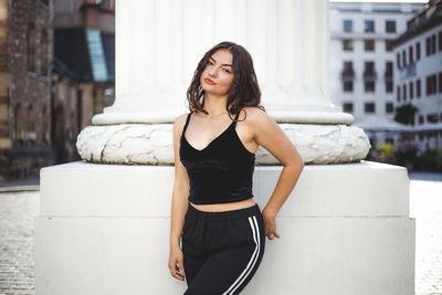 Portrait of young woman standing against pillar in city