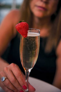 Midsection of mature woman holding champagne flute while sitting in restaurant