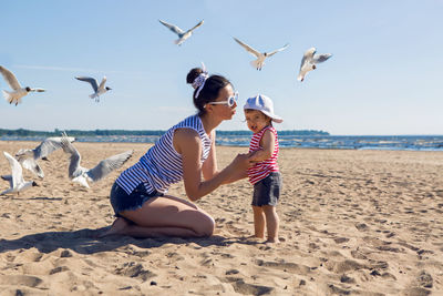 Mother and son sitting on the beach and flying around the birds seagulls