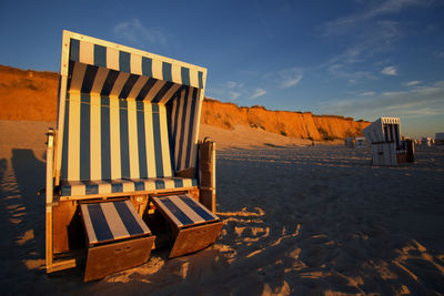 Hooded chairs on beach against red cliff during sunset