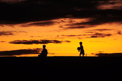 Silhouette boys against cloudy orange sky during sunset