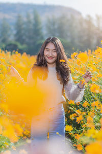 Portrait of woman standing by yellow flowering plants