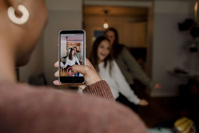 Girl with smart phone filming teenage friends dancing in living room at home