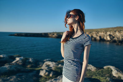 Young woman standing on rock by sea against sky