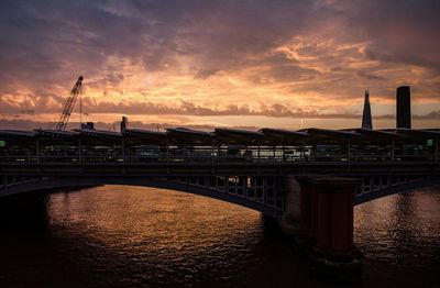 Silhouette of bridge over river against cloudy sky