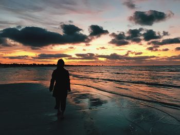 Rear view of silhouette mature woman walking at beach against sky during sunset