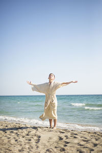 A boy in a muslin robe stands on the seashore with his arms outstretched. faith. transformation.