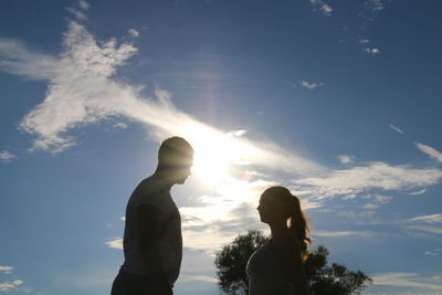 Low angle view of man and woman standing against sky on sunny day