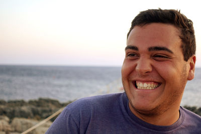 Close-up of smiling man standing by sea against sky