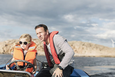 Girl driving motorboat with father in baltic sea against sky