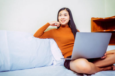 Young woman using phone while sitting on bed at home