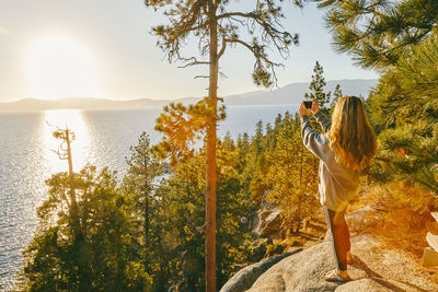 Young woman taking a picture of sunset over lake tahoe.