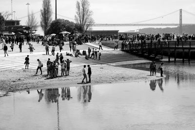 People on riverbank against suspension 25 de abril bridge