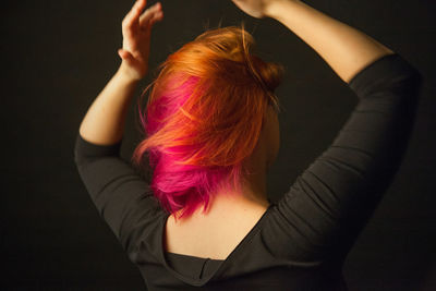 Rear view of woman dancing against black background