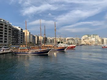 Sailboats moored on river by buildings in city against sky