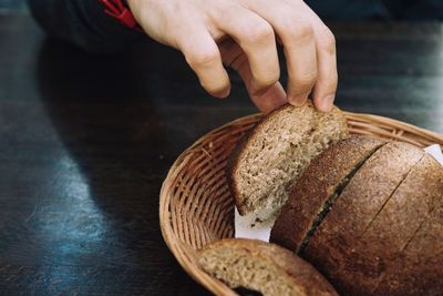 Cropped hand picking bread from basket on table