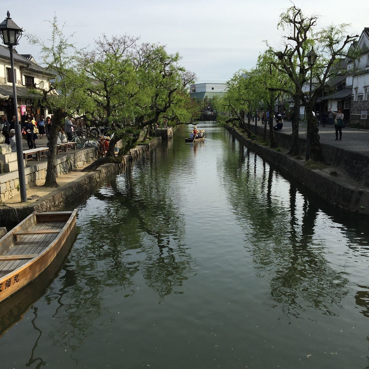 water, tree, building exterior, canal, waterfront, built structure, architecture, reflection, transportation, incidental people, mode of transport, sky, nautical vessel, river, city, day, rippled, outdoors, large group of people