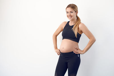 Portrait of smiling pregnant woman standing against white background