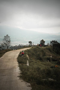 People riding motorcycle on road amidst field against sky