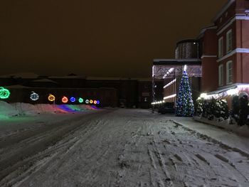 Road amidst illuminated buildings in city at night during winter