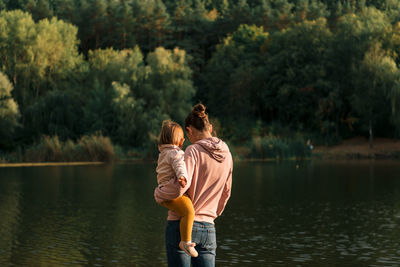 Rear view of mother with daughter standing by lake